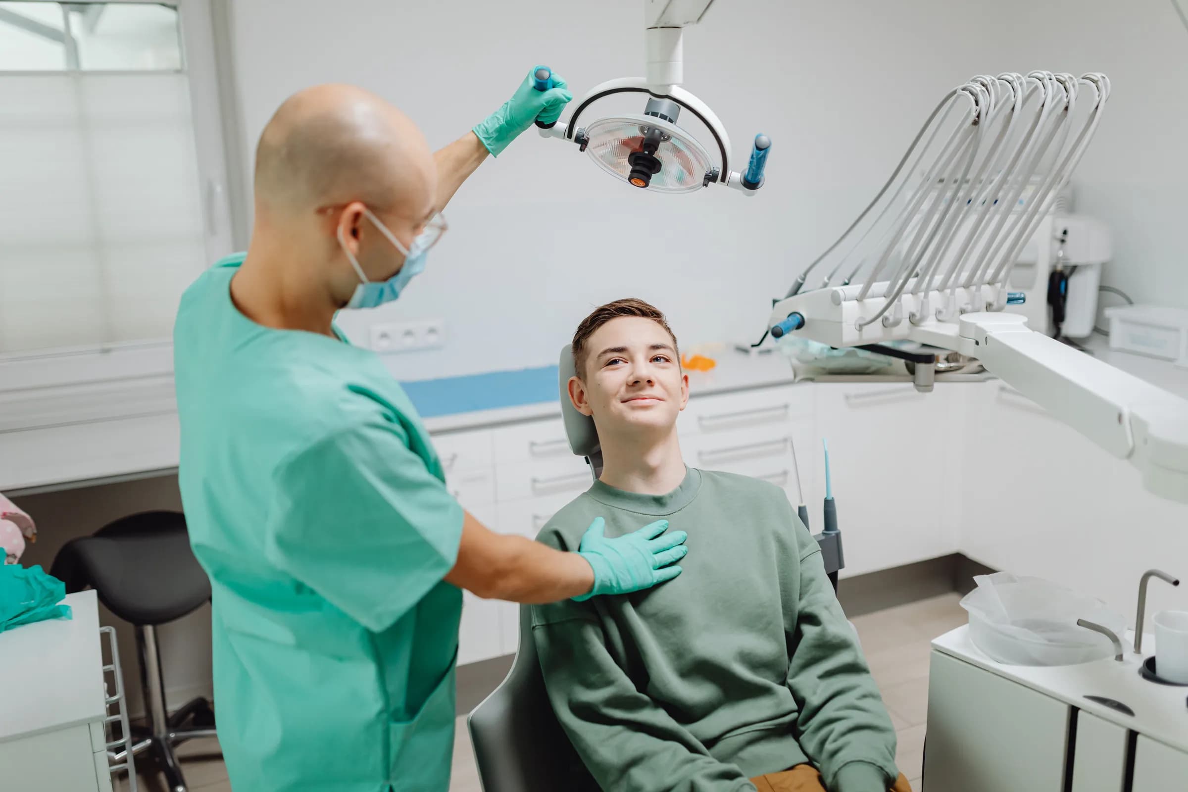 A dentist adjusts the light over a smiling patient in a bright clinic.
